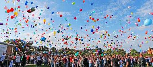 A crowd releasing colorful balloons into the sky, illustrating the theme 'Balloons don't go to heaven'.