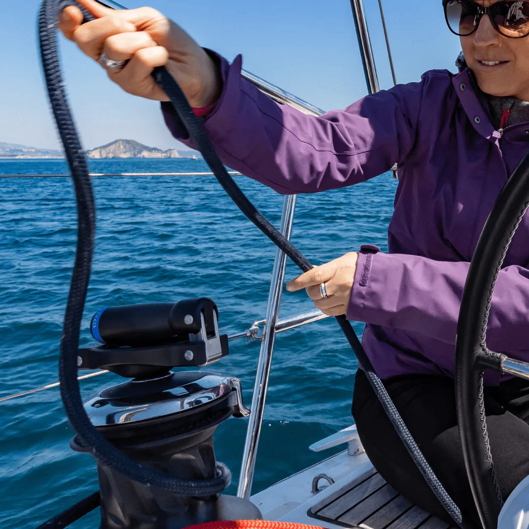 Woman using Folding winch handle EasySea on a sailboat, handling rope near the winch in sunny weather.