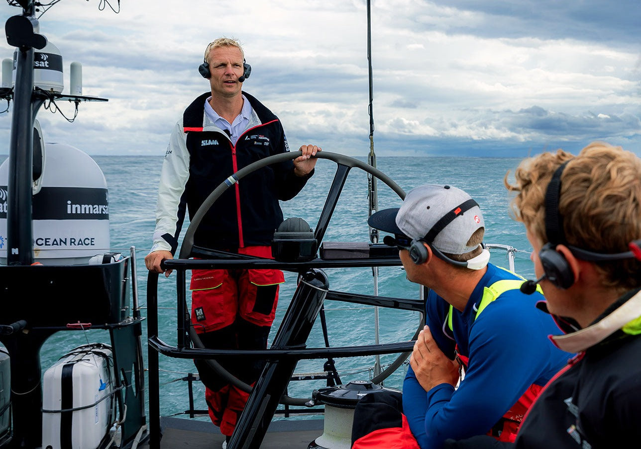 Professional sailing crew using marine communication headsets around the wheel
